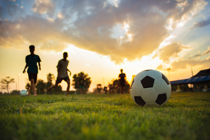 Silhouette action sport outdoors of a group of kids having fun playing soccer football for exercise in community rural area under the twilight sunset sky. action sport outdoors of a group of kids having fun playing soccer football on the dirt field.